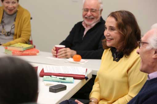 Senior woman speaks with others seated around her.