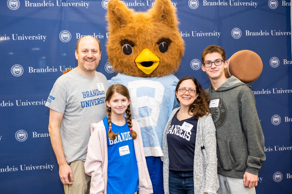 Family standing with Ollie the owl at Alumni basketball event e