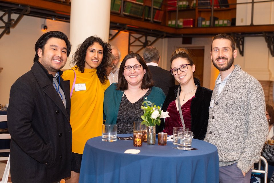 Five alumni standing around a table at a holiday reception.