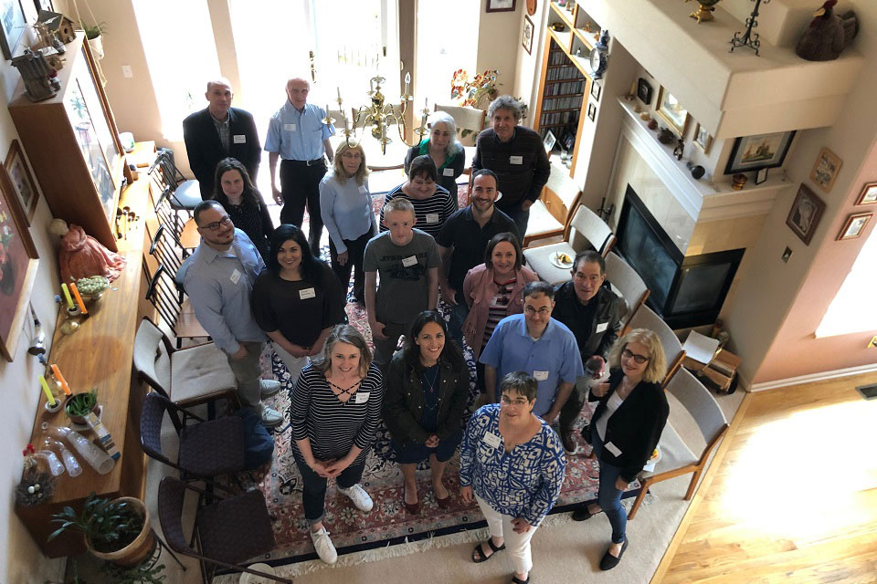 A group of event attendees stand in a living room, looking up toward the camera above.