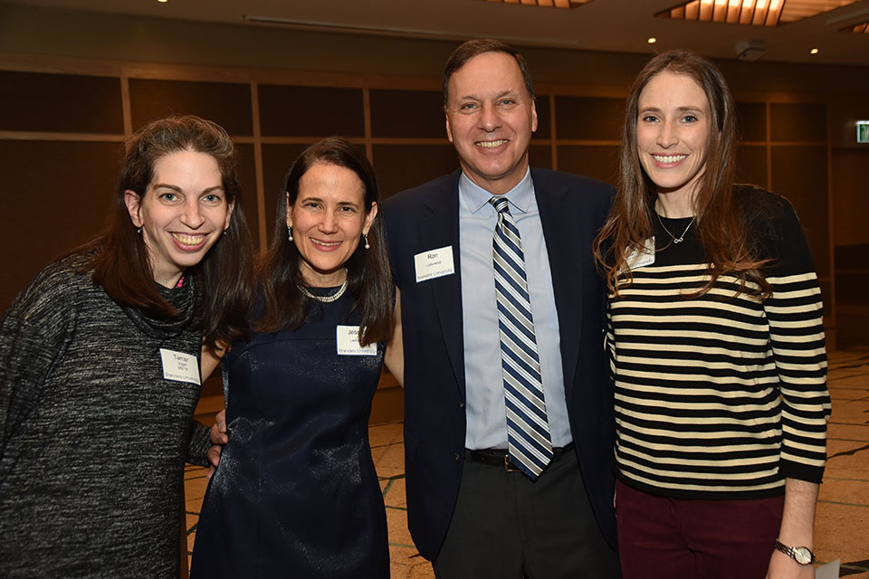 Two women alumni stand on either side of Brandeis president Ron Liebowitz and his wife Jessica. 