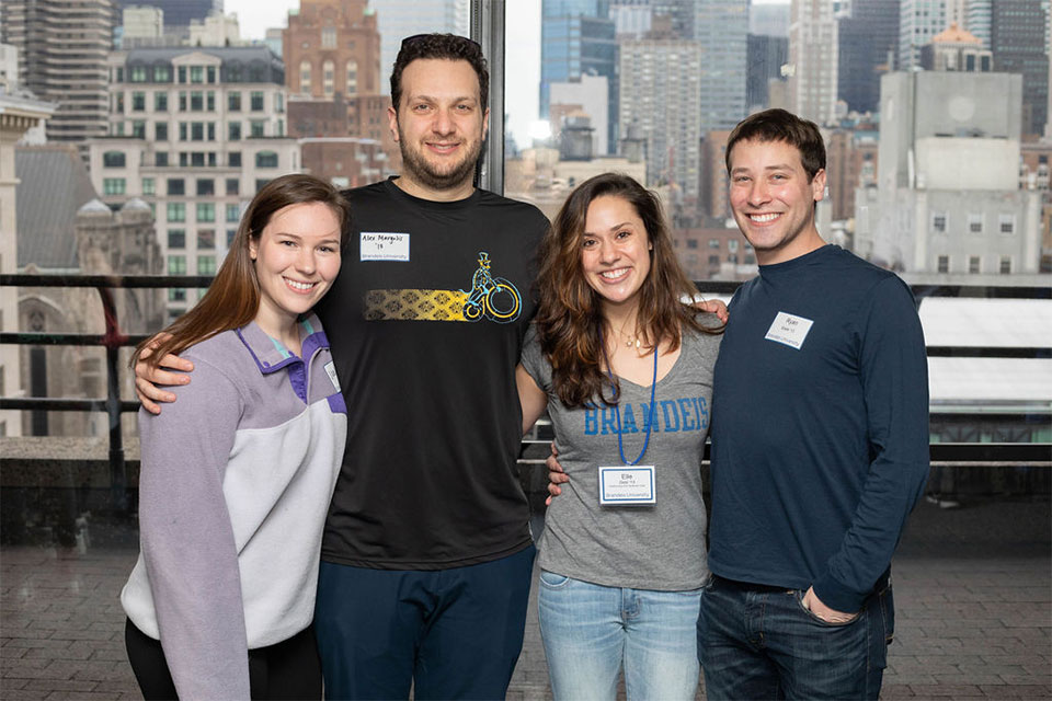 attendees wearing Brandeis gear in front of window with views of NYC skyline
