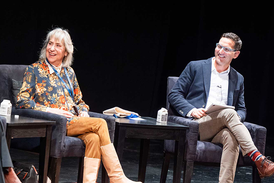 Two people smile on stage during an event.