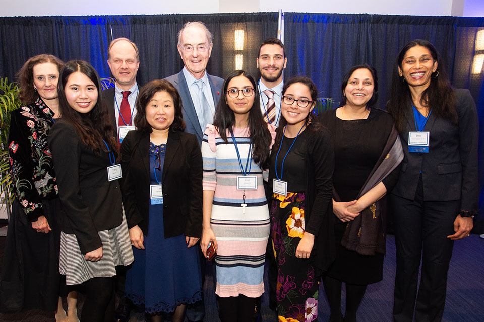 Peter Malkin and a group of alumni standing together in front of a blue backdrop.