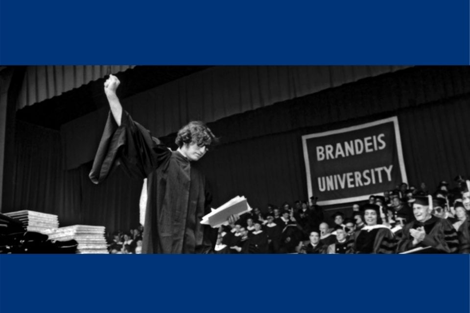 A black and white folder of a Brandeis graduate holding their fist in the air while walking across a stage