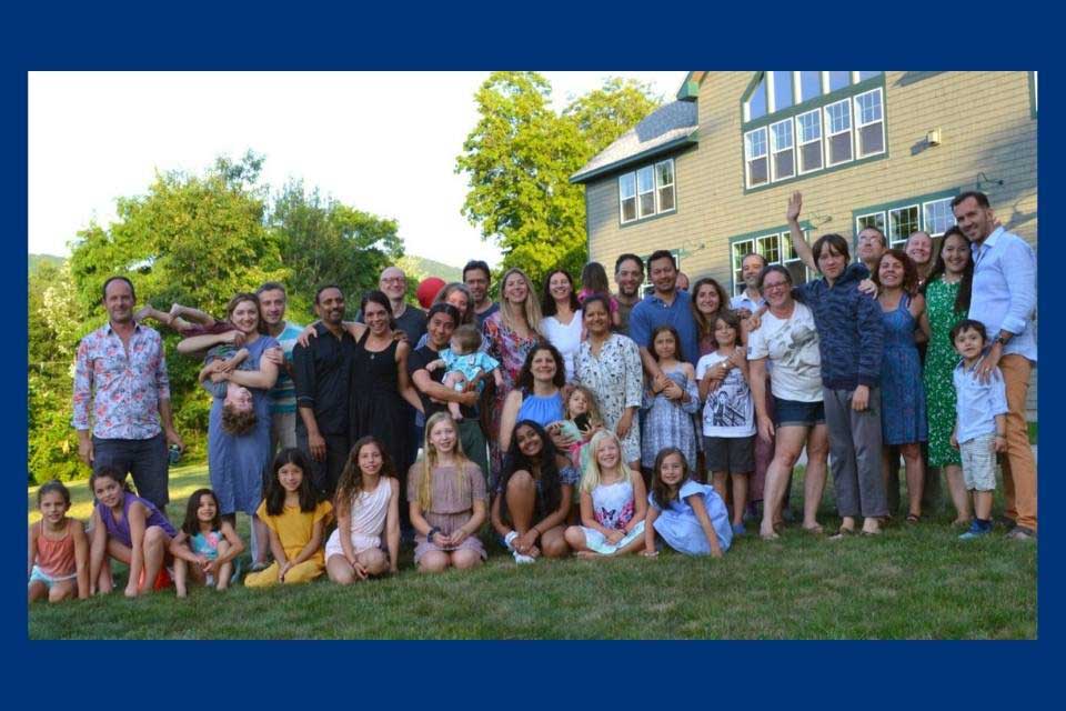 Large group of alumni and their families posing outside in front of a large home. 