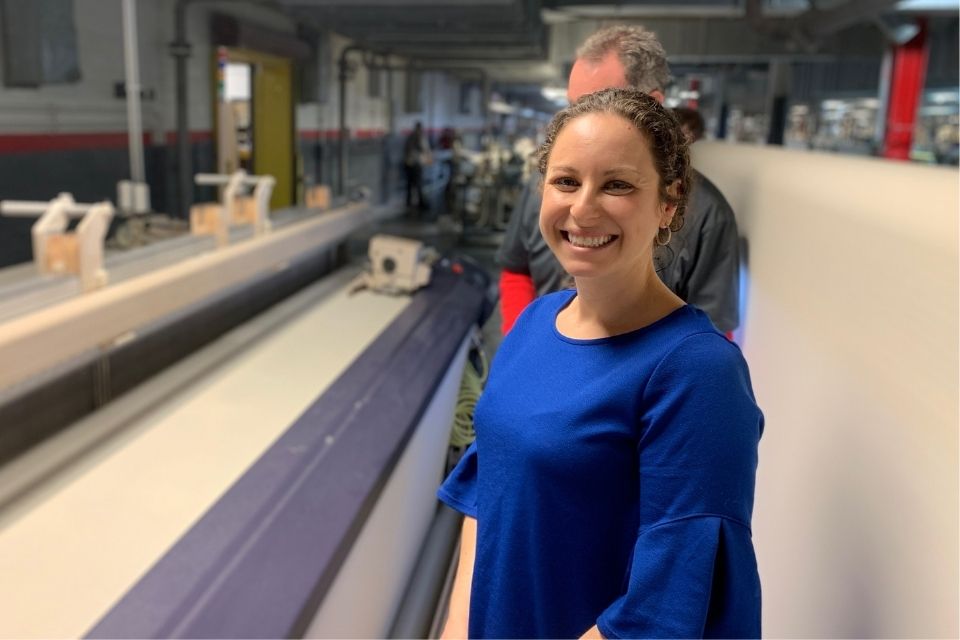 Stephanie Fodor MacDonald stands in a textile warehouse and smiles