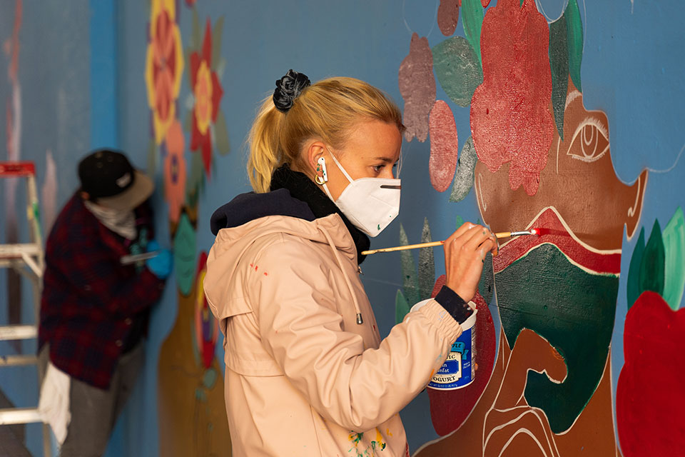 Amelie de Cirfontaine wearing a medical mask and painting a mural.
