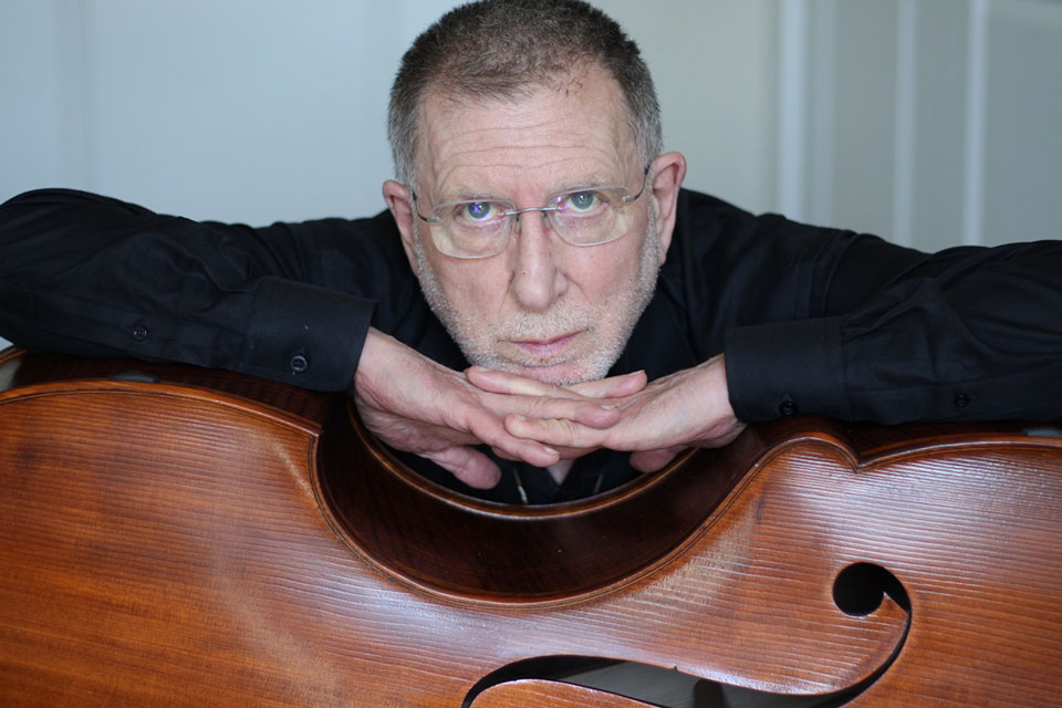 Chuck Israels leaning his head on his hands on the side of an upright bass.