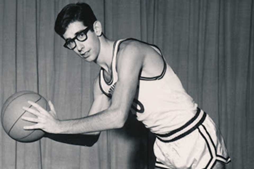 Mike Leiderman in a Brandeis basketball uniform, posing with the ball. 