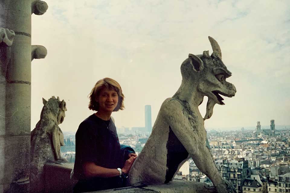 Mara Posner Metzger stands next to a gargoyle atop Notre Dame cathedral.