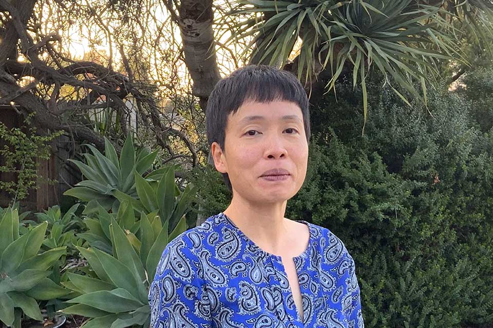 Ming Lee Tang smiling in front of a background of green plants and foliage