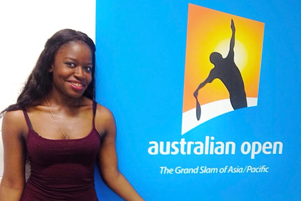 Linda Phiri smiling while standing next to an Australian Open sign at Melbourne Park. 