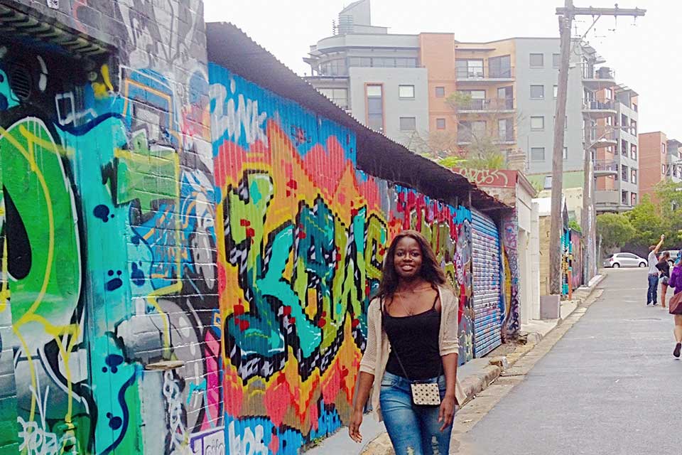 Linda Phiri walks by colorful graffiti filled walls in Newtown, Australia