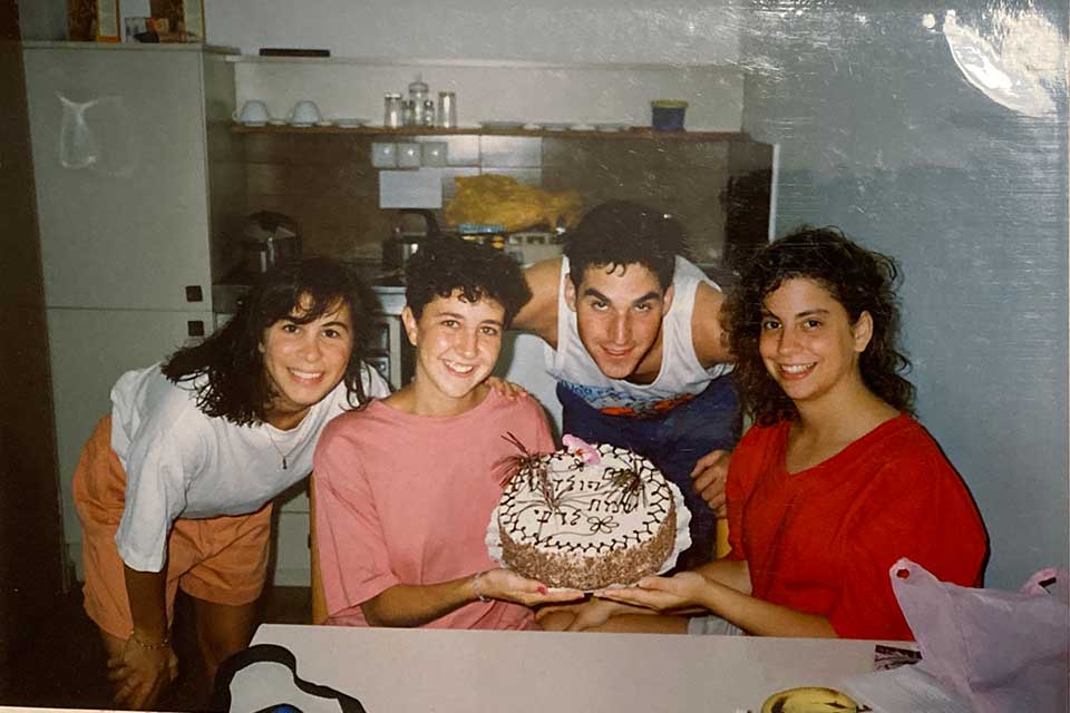 Steve Safran smiling with three women holding a birthday cake with Hebrew writing