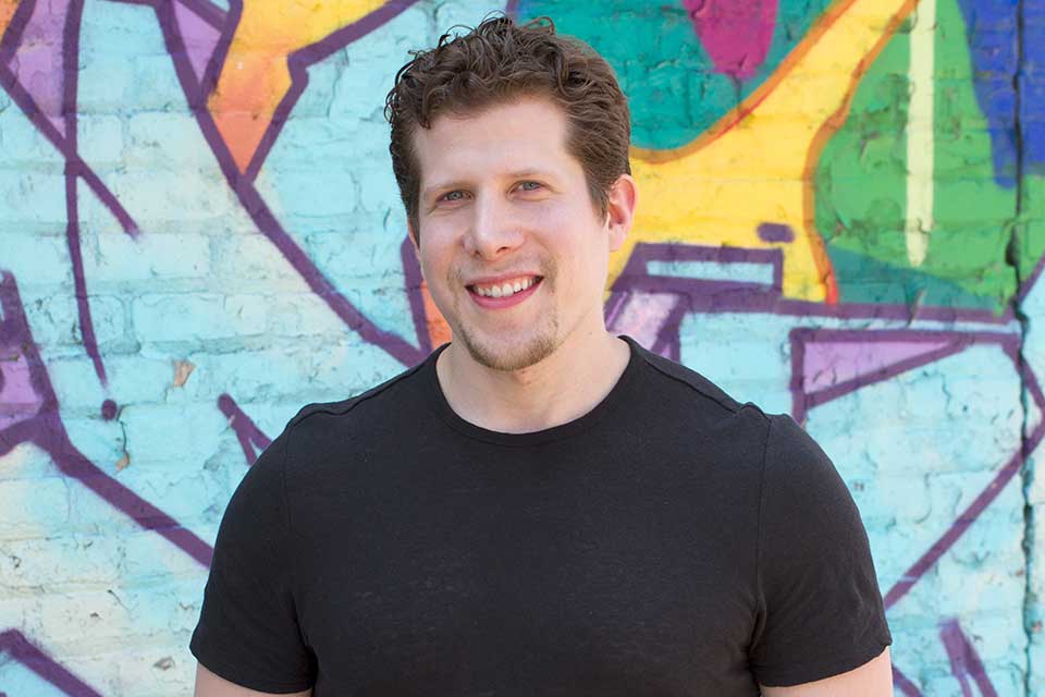 Michael Shoretz in black t-shirt standing in front of a wall with graffiti