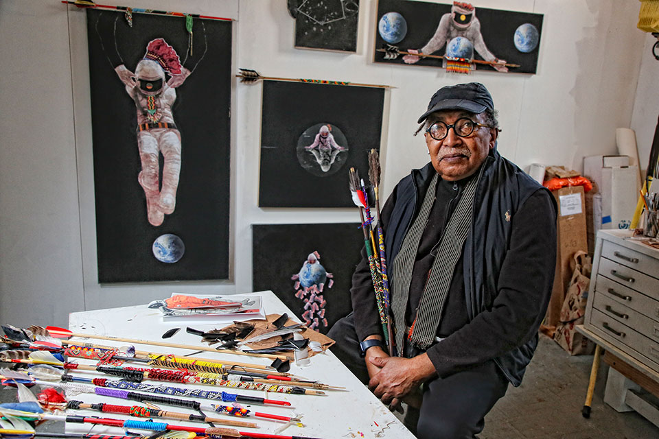 Ari Montford sitting in his studio with paintings 