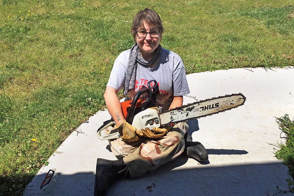 Laura Block sitting on the ground with a chain saw on her lap. 