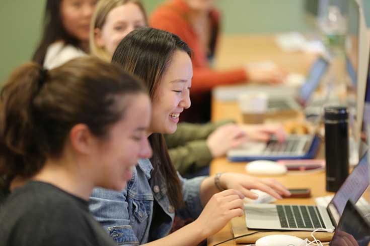 female students in classroom smiling while looking at laptops