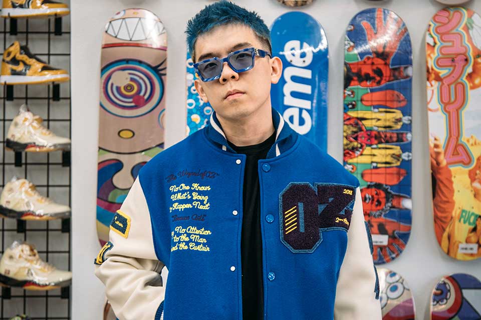 Jiahuan Green Xia with blue hair and sunglasses in front of a wall of sneakers 