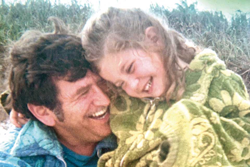 Kama Einhorn as a child, hugging her father as they both smile.